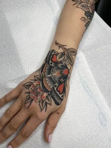Moth and flowers across the hand — traditional tattoo by Alex Roze, Kelowna